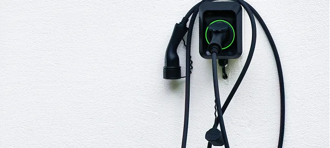 Wallbox mit eingestecktem Ladekabel an einer weißen Hauswand