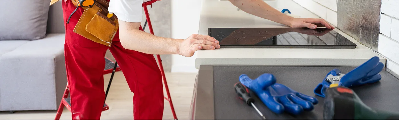 Handwerkerin montiert ein Induktionskochfeld in eine Küchenarbeitsplatte