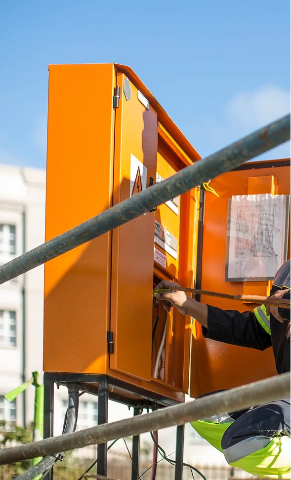Monteur schließt einen orangefarbenen Baustromverteiler am Gerüst an