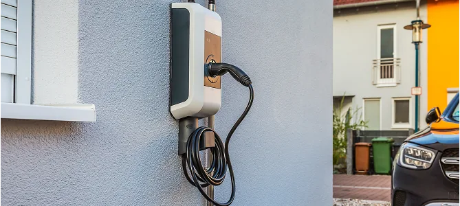 Wallbox mit Ladekabel an der Fassade, daneben geparktes Auto