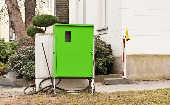 Grüner Baustromverteiler auf Rollgestell vor einem Wohnhaus